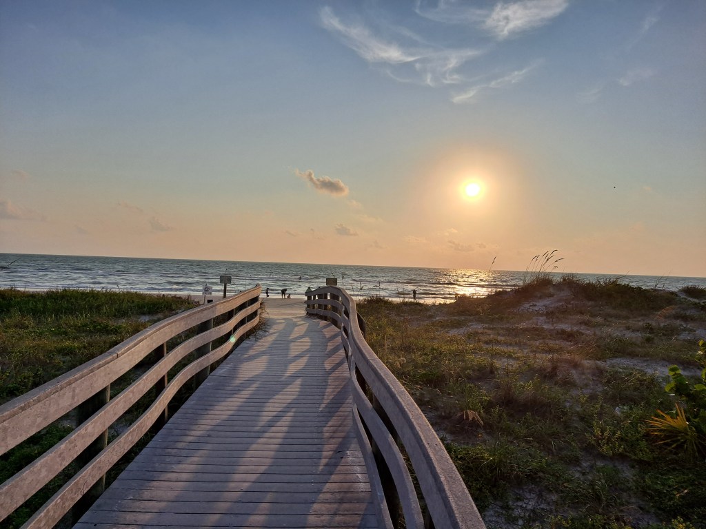 Sunset over a quiet beach boardwalk, symbolizing a reflective journey and gentle transition into evening.